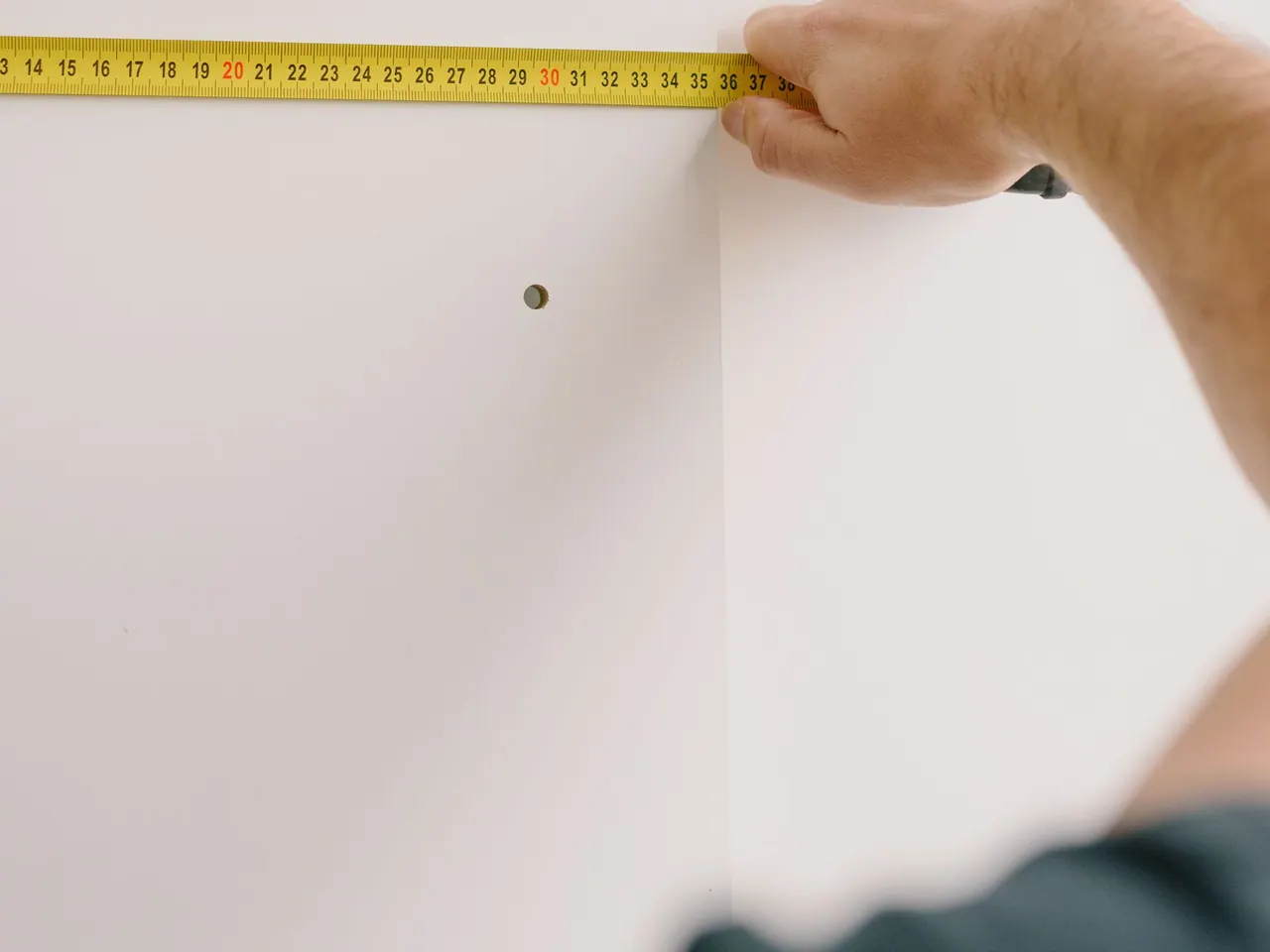 Hand mit Maßband misst eine weiße Wand aus