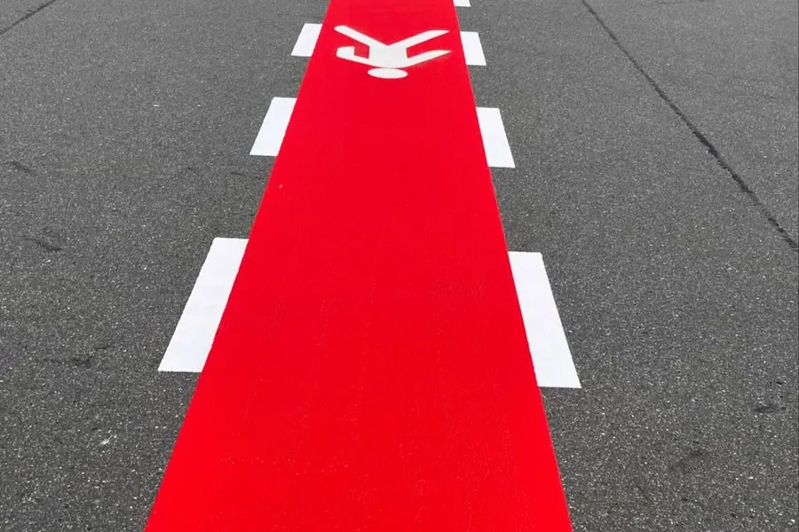 Rot markierter Fußgängerweg mit weißen Randlinien und Piktogramm auf einem Betriebshof