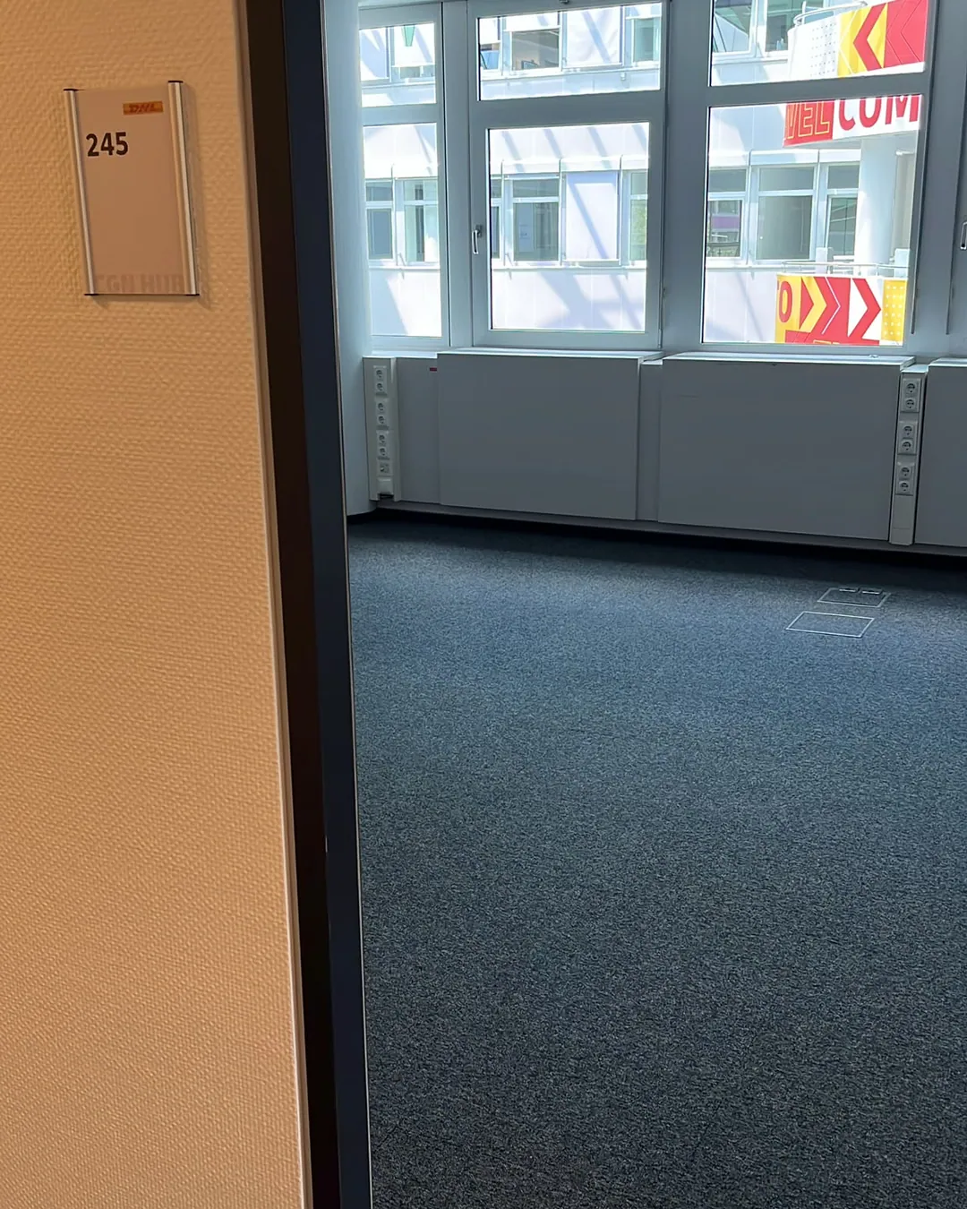 Büro mit neuem grauem Teppichboden, weißen Wänden und Glastür