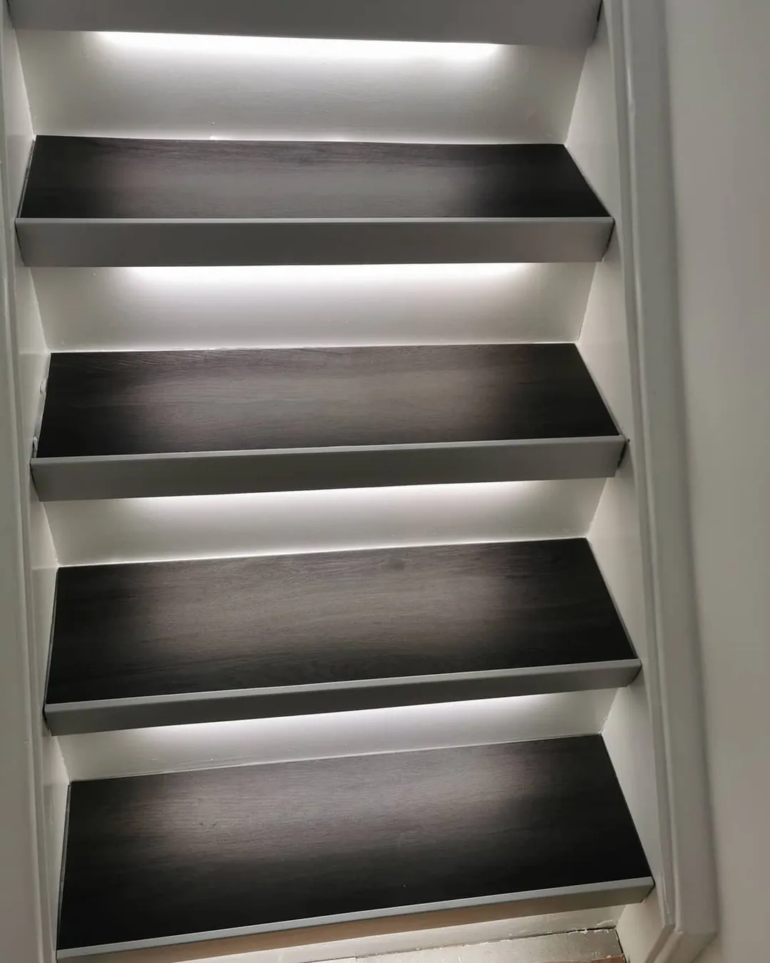 Nachher: Dieselbe Treppe erneuert: dunkle Stufen, weiße Setzstufen und LED-Lichtleisten